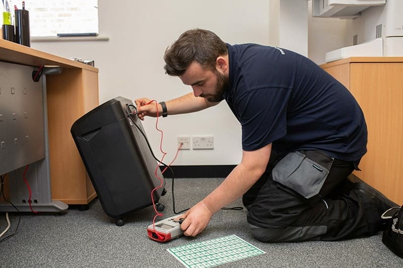 Qualified engineer carrying out PAT testing in a school classroom